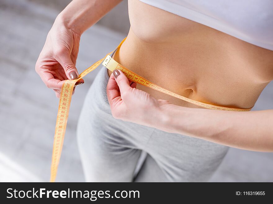 Waist size. Nice slim woman holding a centimeter tape while measuring her waist. Waist size. Nice slim woman holding a centimeter tape while measuring her waist