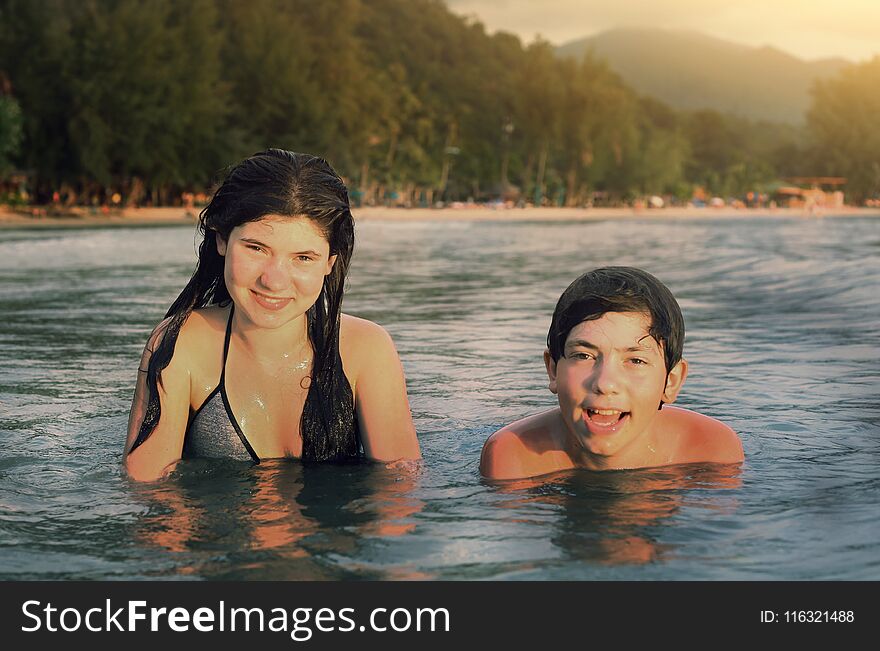 Teenager siblings couple brother and sister swimming in the sea on palm beach background