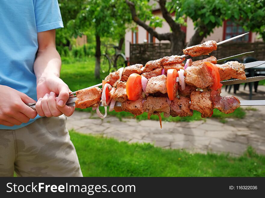Raw barbecue on skewer in the hands of young man. Sunny spring day, closeup view.