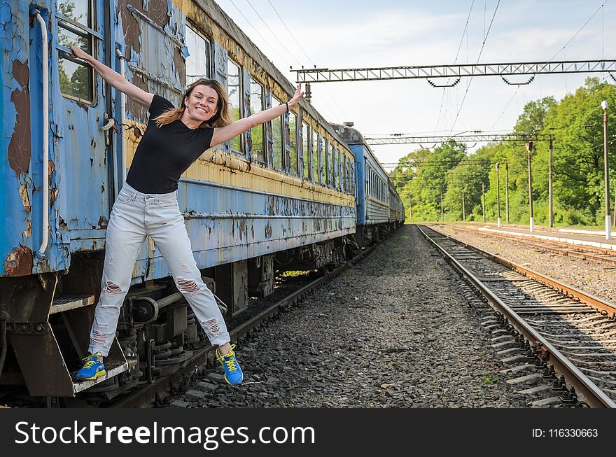 A young beautiful girl is standing on the step of an old railway carriage, a departing train