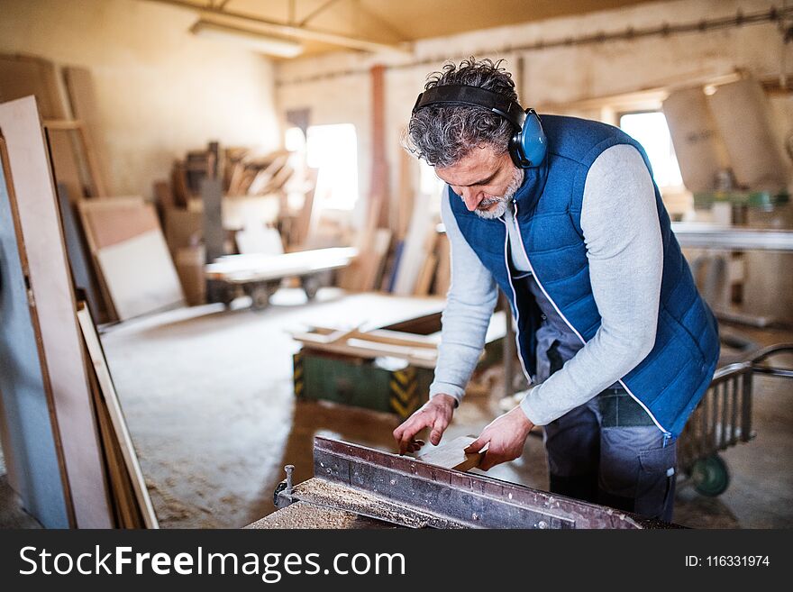 A mature man worker in the carpentry workshop, working with wood.