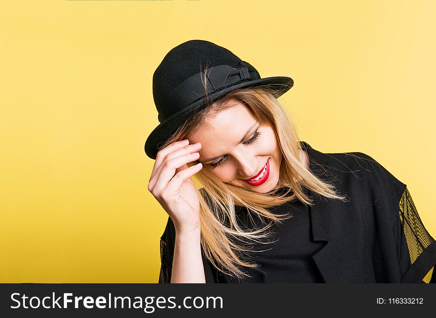 Portrait of a young beautiful woman with black hat in studio on a yellow background.