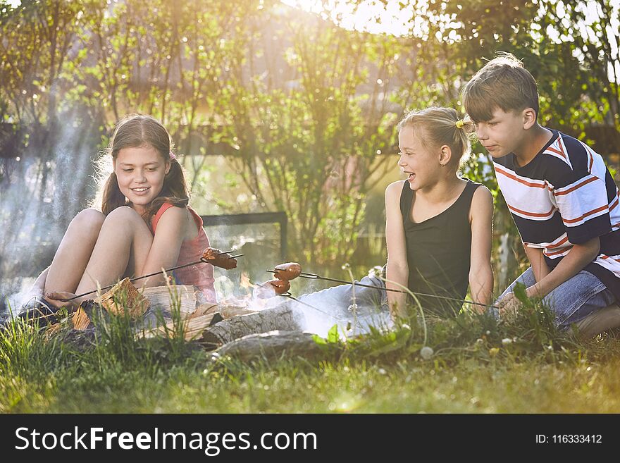 Children enjoy campfire. Siblings family toasting sausages on the garden at sunset.