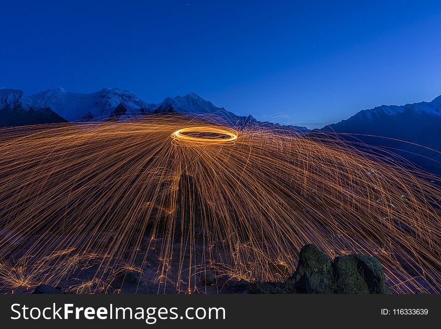 Fire show on the top of hill with snow mountain background at dusk.