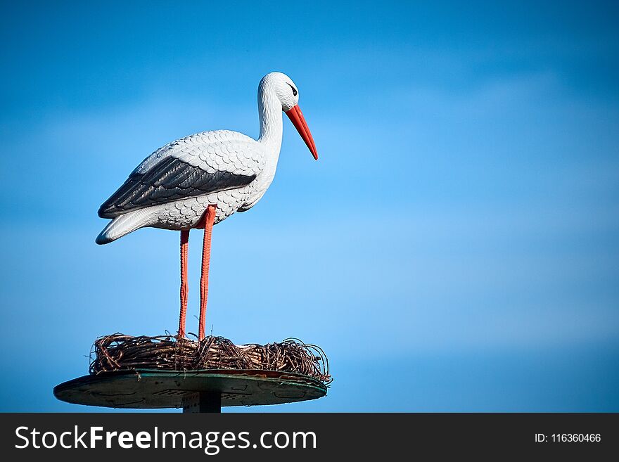 Decorative stork sits in a nest against the blue sky on a garden plot. Decorative stork sits in a nest against the blue sky on a garden plot