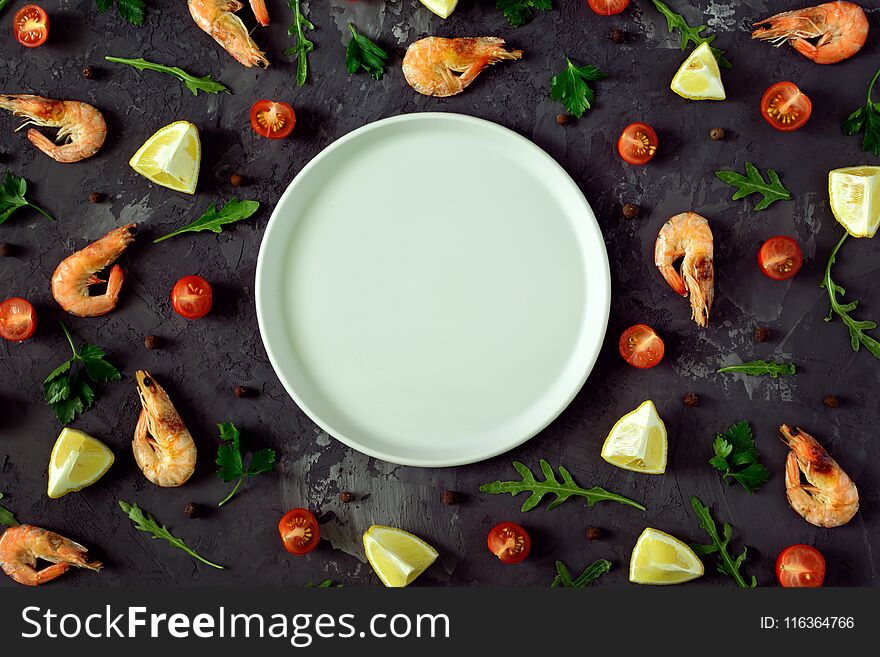 In the center of a dark textured background an empty gray plate, a mock-up. Around are scattered lemon, herbs, spices and shrimp. Beautiful photos from the top, mock up.