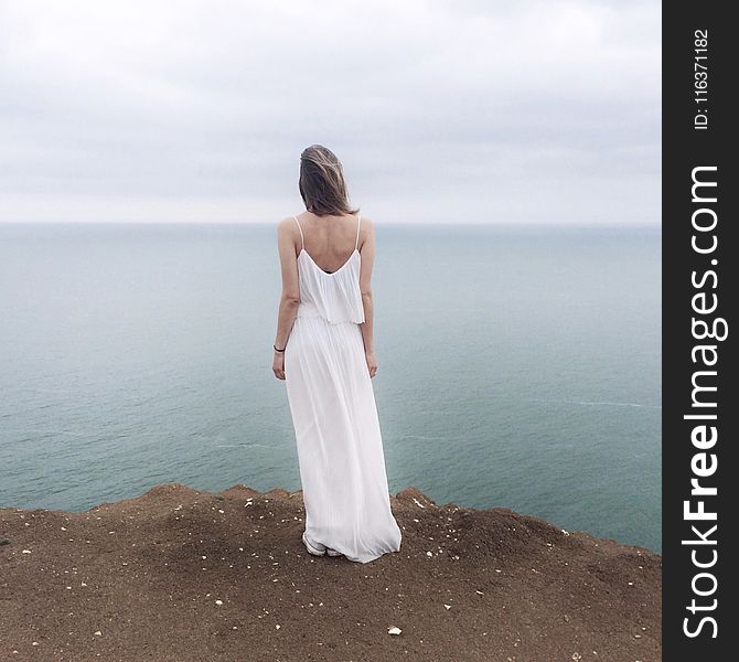 Woman in White Spaghetti Strap Dress Standing on Cliff