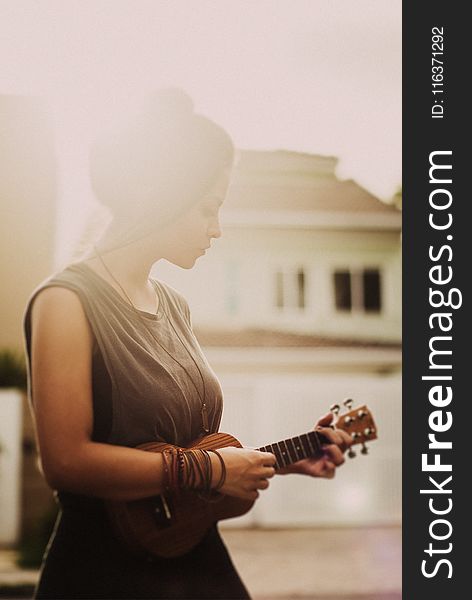 Woman In Brown Sleeveless Dress While Playing Ukulele