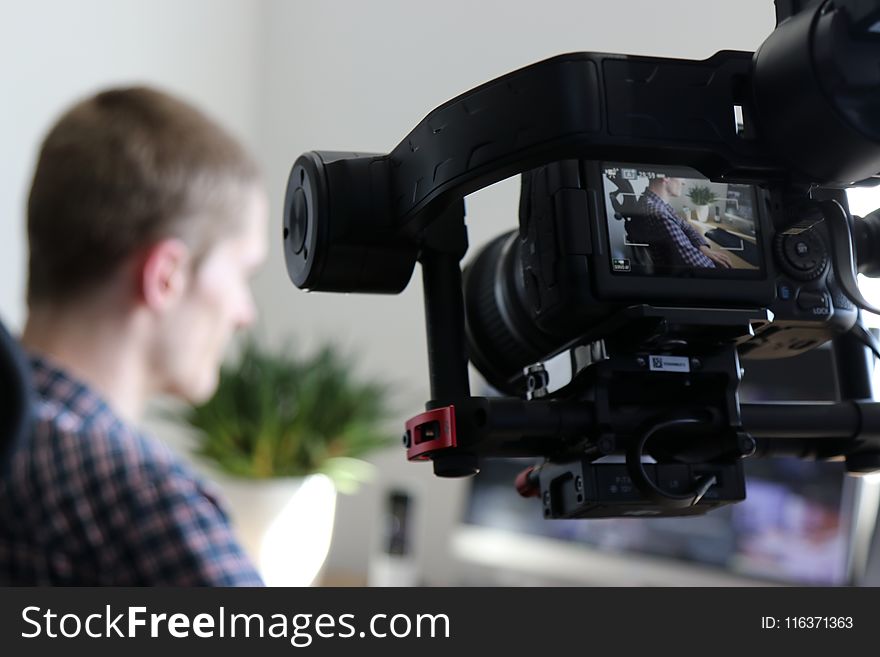 Black Video Camera Turn On Next To Man Wears Black And Gray Shirt