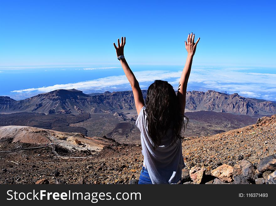 Woman Standing on Mountain While Raising Her Hands