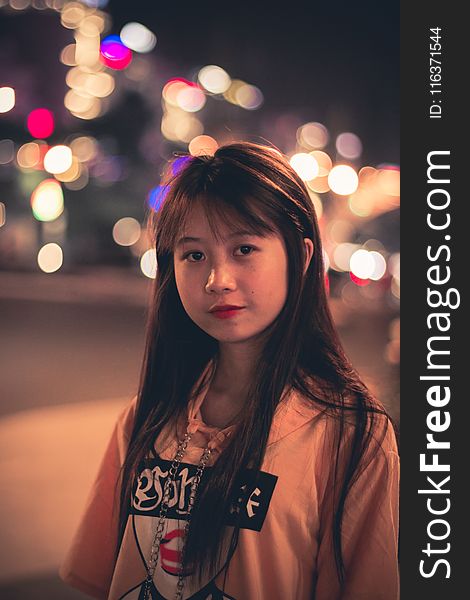 Woman Wearing Pink, Black, and Red Printed Pullover Hoodie Standing Beside Road Bokeh Photography at Night Time