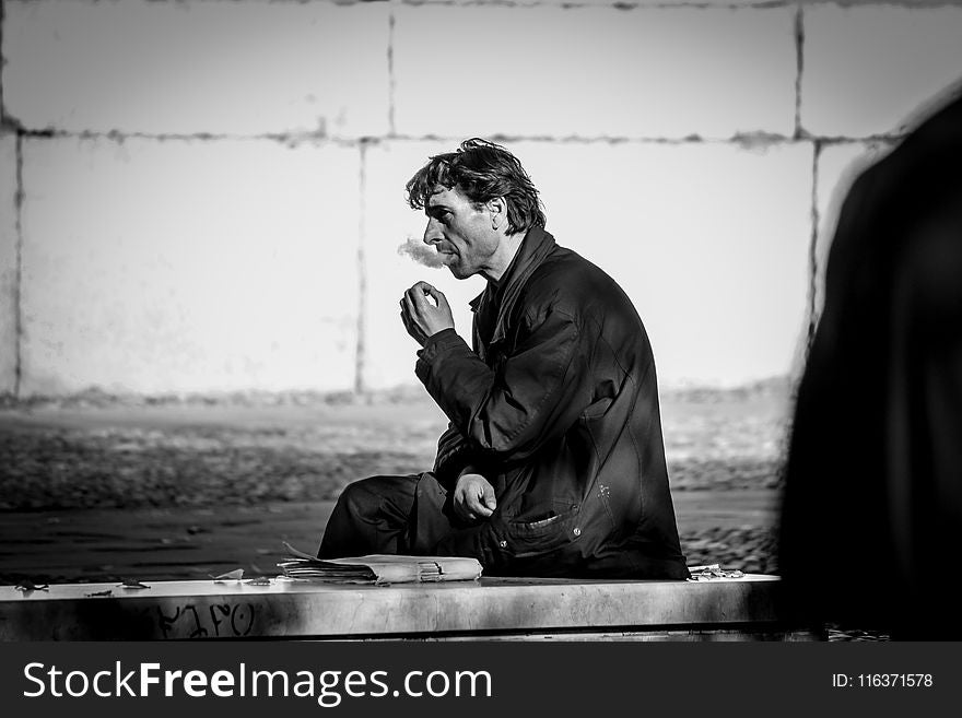 Grayscale Photo of Smoking Man While Sitting on Bench