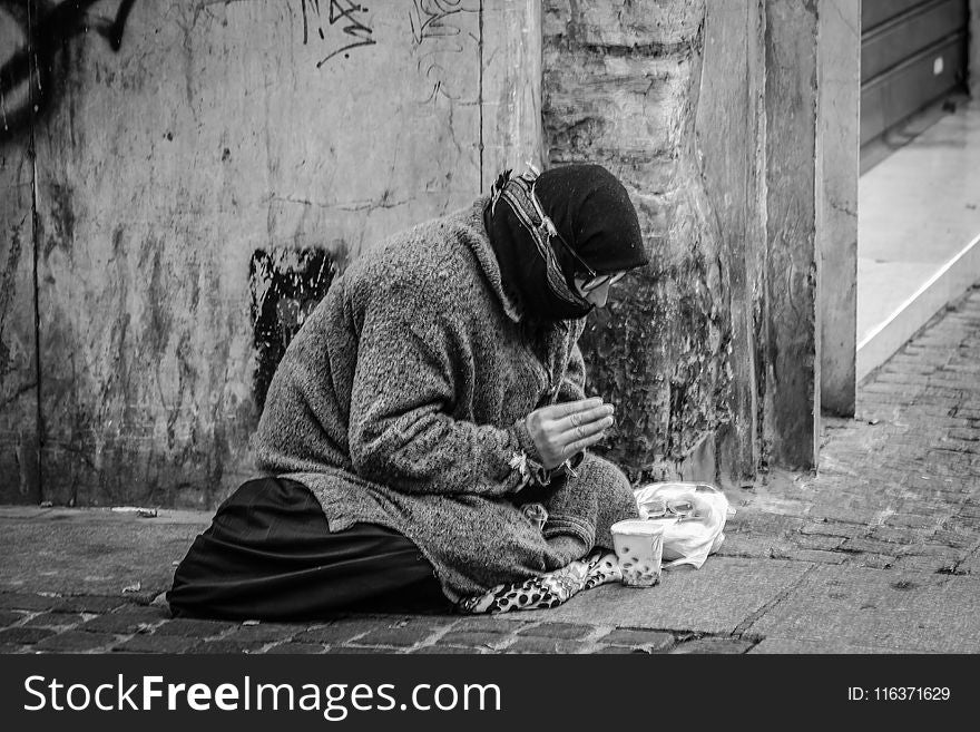 Grayscale Photography of Man Praying on Sidewalk With Food in Front