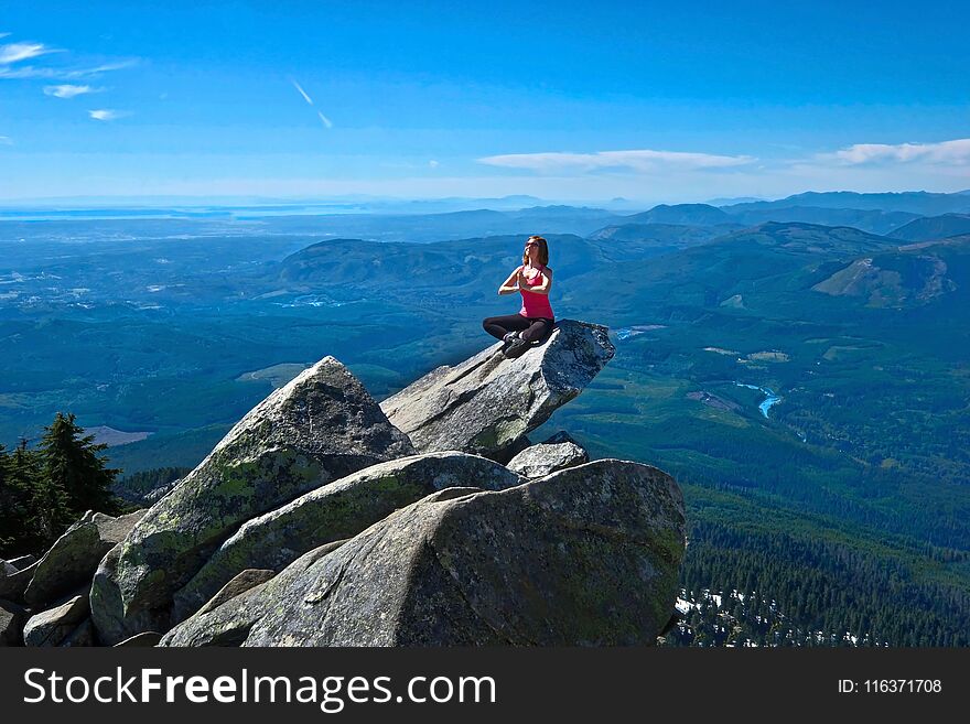 Young woman meditate on rock above beautiful valley.