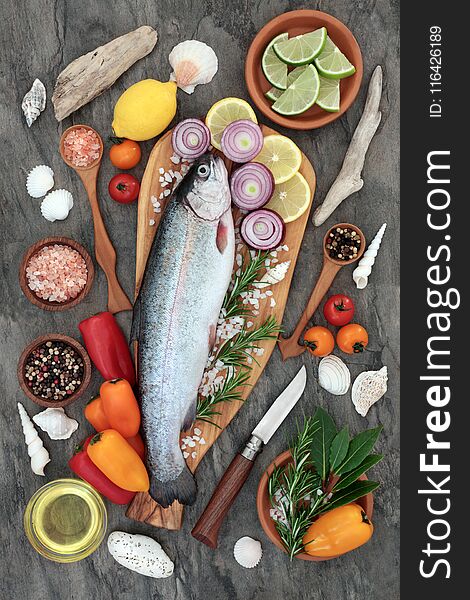 Healthy heart food with rainbow trout fish, seasoning, herbs, vegetables and olive oil on marble background. High in omega 3 fatty acids.