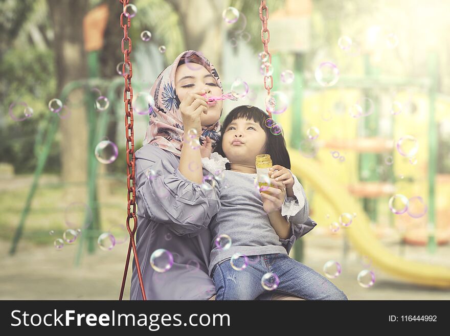 Muslim woman with child blowing soap bubbles
