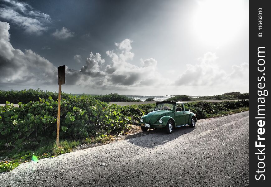 A green classic car in a sea landscape during sunset. A green classic car in a sea landscape during sunset.