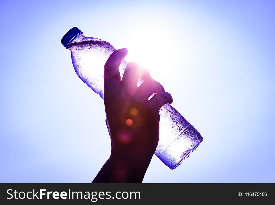 Silhouette of closeup Woman`s hand holding plastic water bottle over sunlight effect. World Water Day concept.