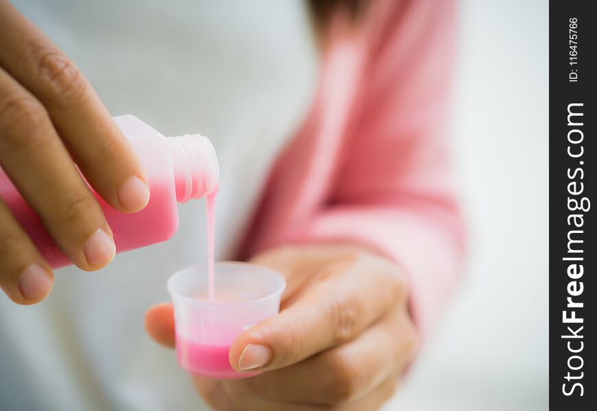 Closeup woman pouring medication or antipyretic syrup from bottle to cup. Healthcare, people and medicine concept -