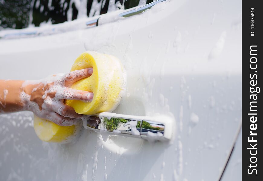 Woman hand with yellow sponge washing car.