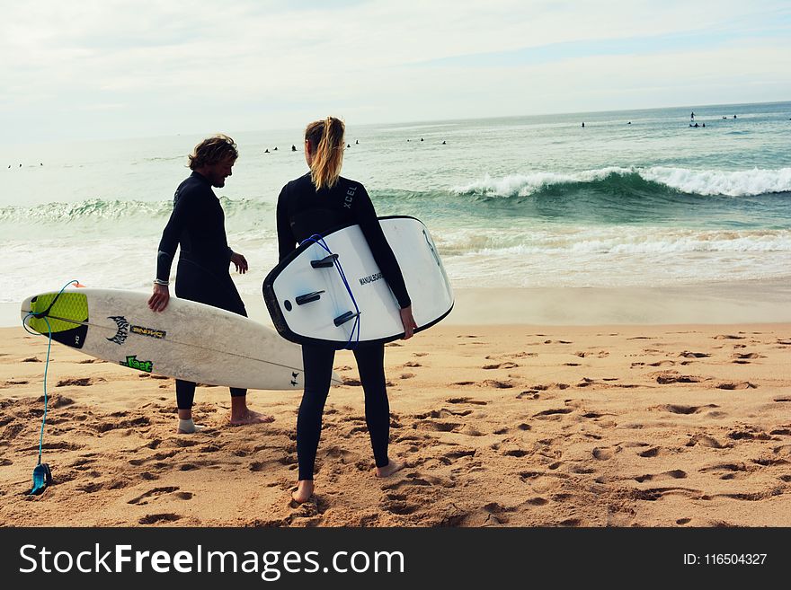 Man and Woman Holding Surfboards on Seashore