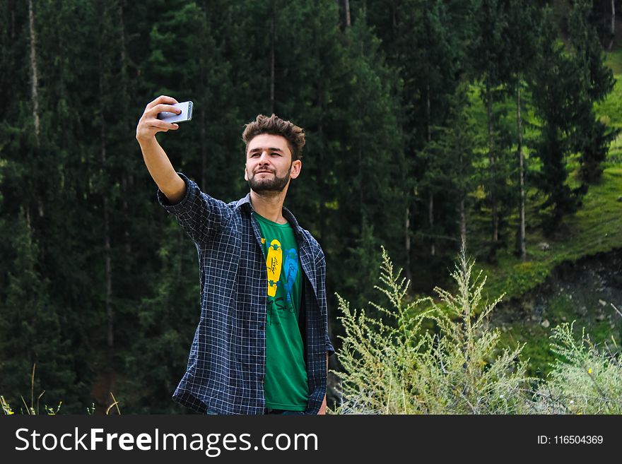 Man in Blue Sports Shirt and Green Top Taking a Selfie Near Green Trees