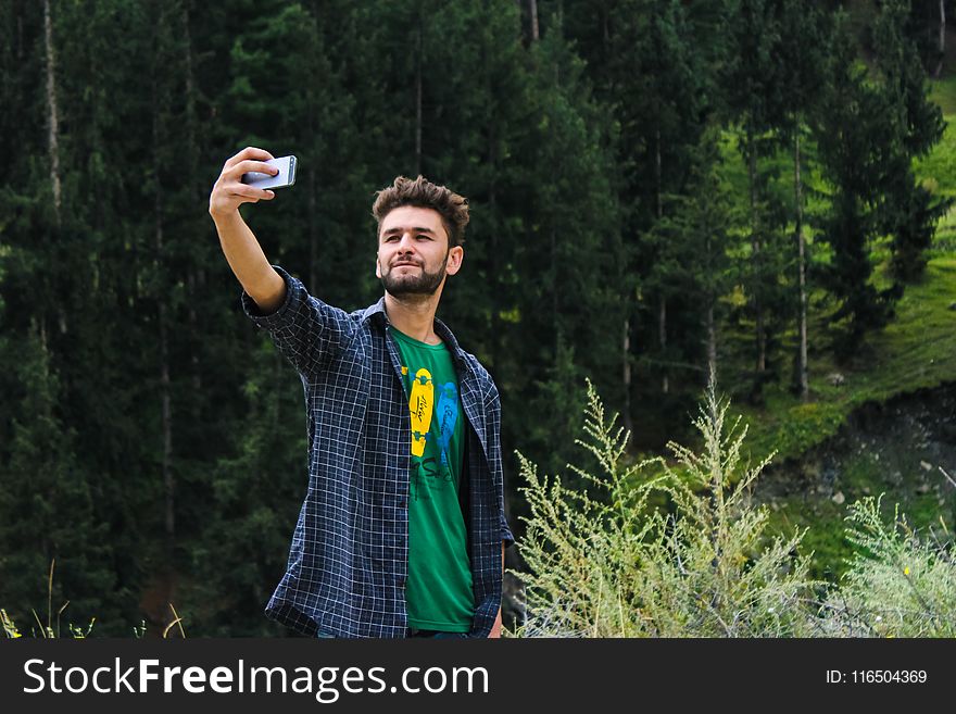 Man In Blue Sports Shirt And Green Top Taking A Selfie Near Green Trees