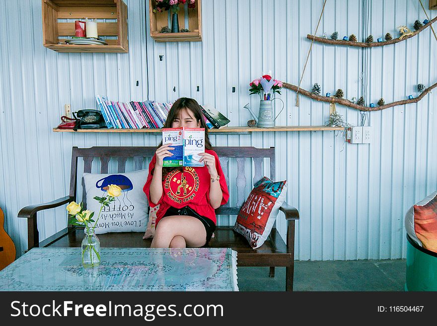 Woman in Red Shirt Holding Book Sitting on Bench in Front of Coffee Table