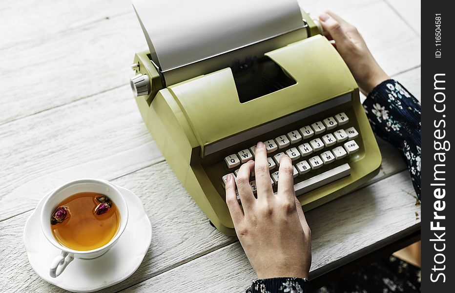 Person Holding Type Writer Beside Teacup and Saucer on Table
