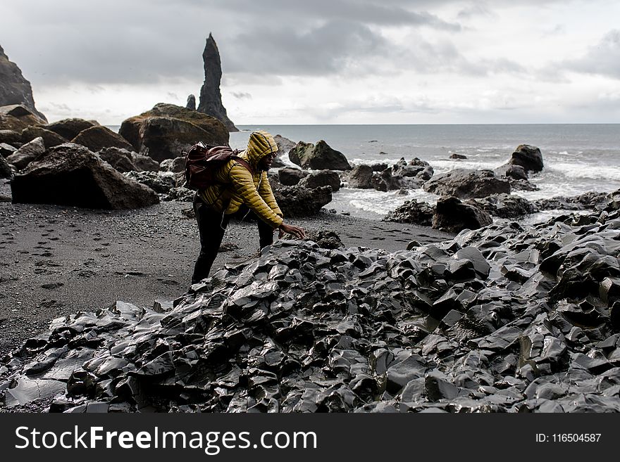 Person Wearing Hoodie Touching Stone in Seashore