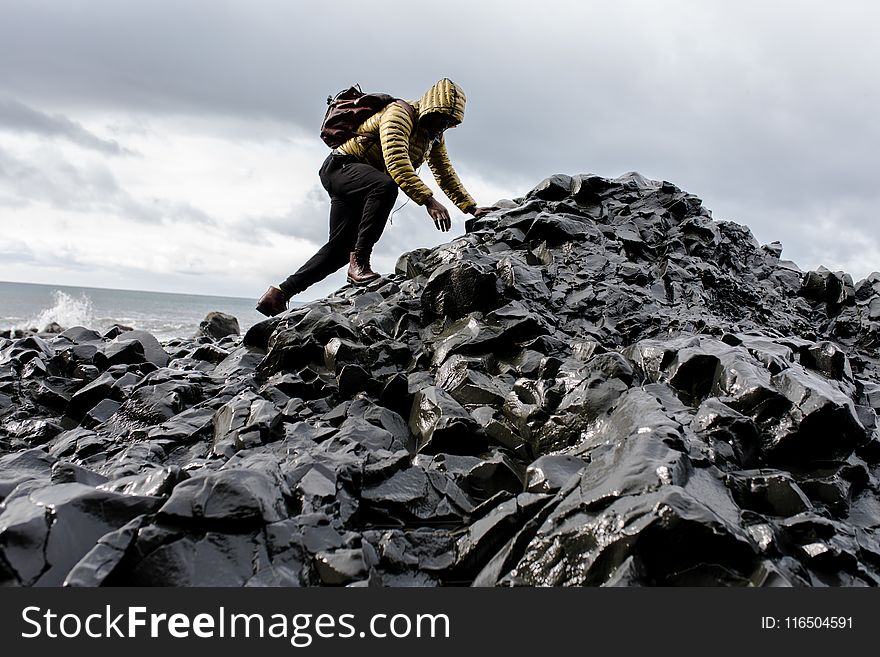 Man Wearing Hoodie and Black Pants Climbing Up Pile of Rocks