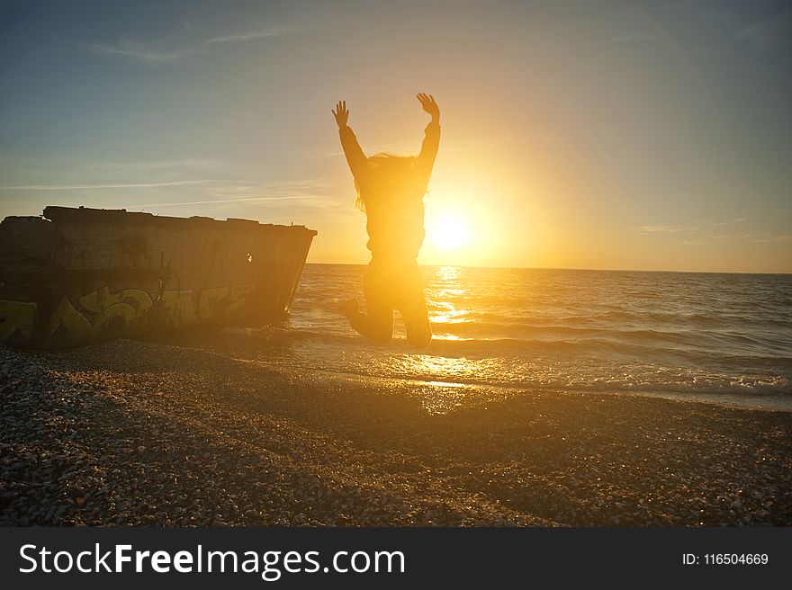 Person Jumping on Seashore during Golden Hour