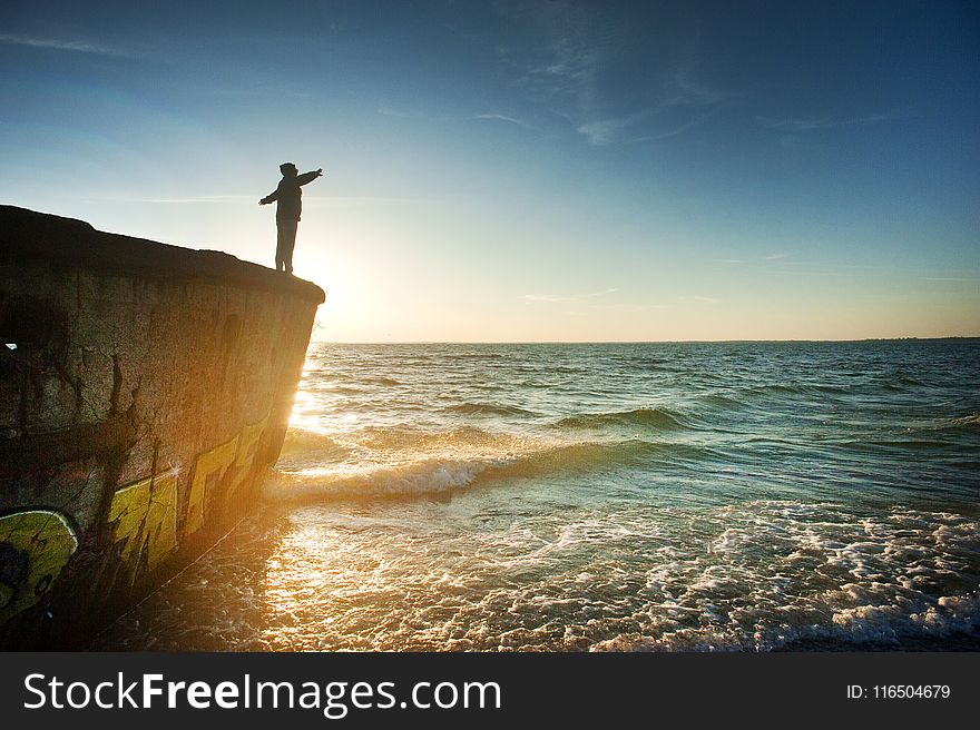 Silhouette Of Person On Cliff Beside Body Of Water During Golden Hour