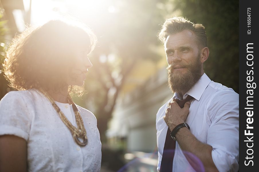 Man Holding His Necktie While Looking at Woman Wearing White Top