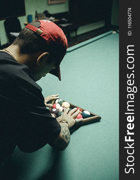 Man in Black T-shirt and Red Baseball Cap Arranging Billiard Balls on Table