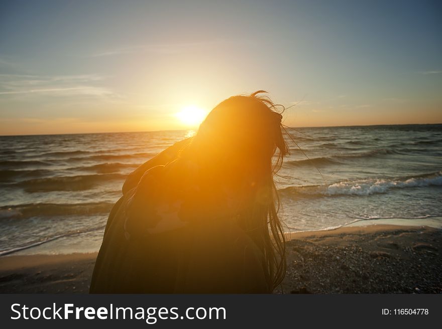 Silhouette Of Woman Sitting On Beach Shore