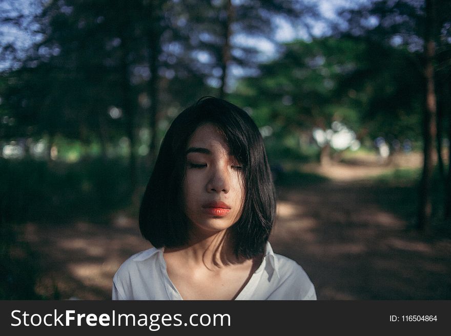 Shallow Focus Photography of Woman in White Top Beside Green Trees