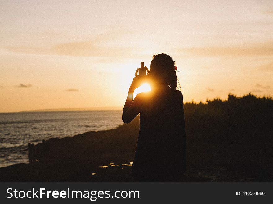 Silhouette of Woman Standing Near Body of Water during Sunset