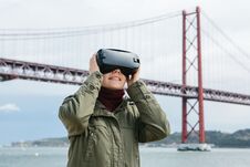 Young Beautiful Girl Wearing Virtual Reality Glasses. 25th Of April Bridge In Lisbon In The Background. The Concept Of Royalty Free Stock Images