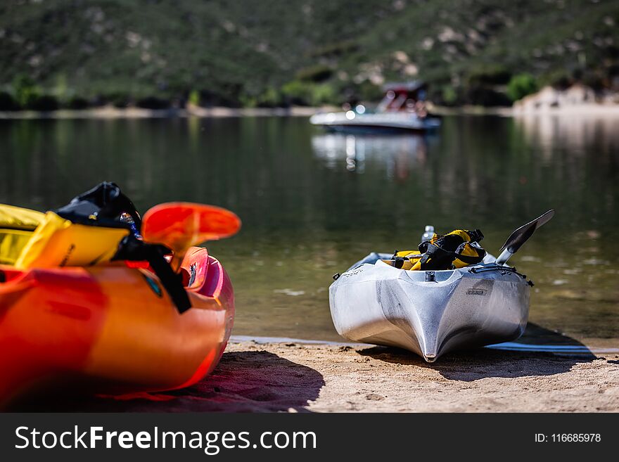 A pair of Kayaks beached on the shore of a lake in the summer time