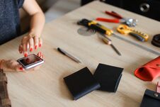 Female Hands With Red Nails At Leather Atelier Using Smartphone, Handmade Wallets And Tools On Table. Stock Image
