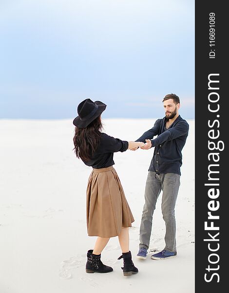 Young woman wearing skirt nad hat holding hands of handsome man on snow in white background.