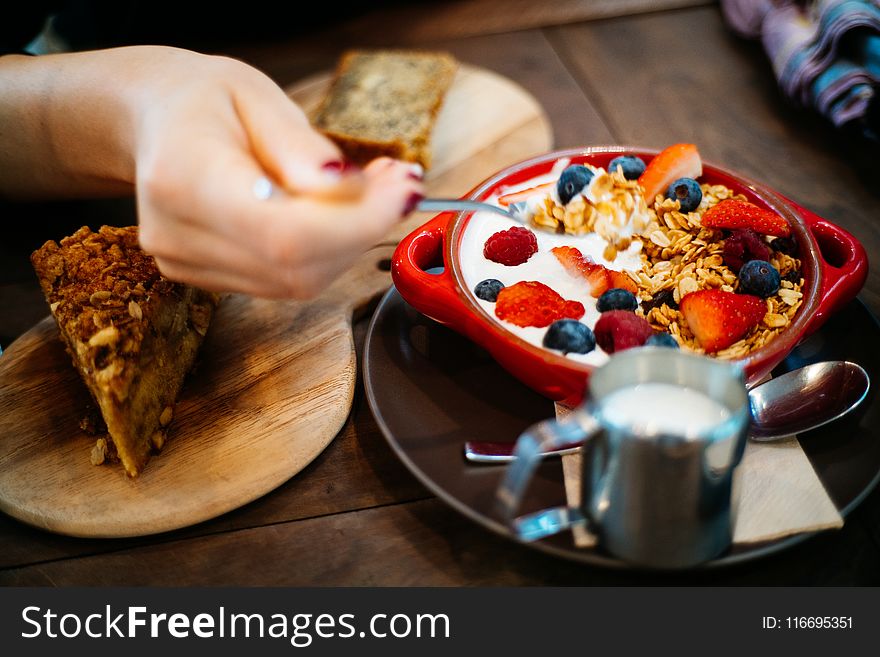Person Holding Spoon and Round Red Ceramic Bowl With Pastries
