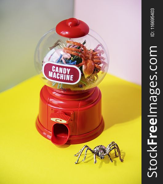 Red and Clear Plastic Candy Machine on Yellow Desk