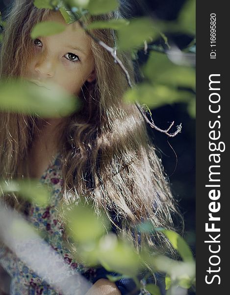 Woman Wearing Multicolored Floral Top Behind Green Leaf Plant