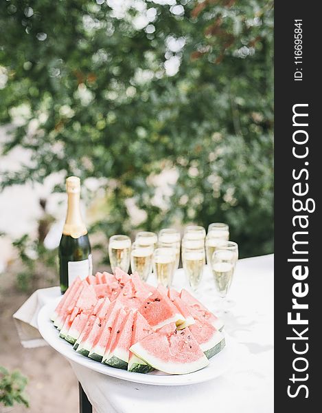 Selective Focus Photo of Bunch of Sliced Watermelons in White Bowl Near Champagne Bottle
