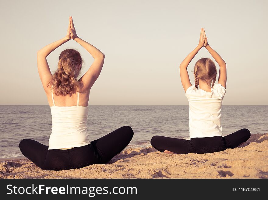 Mother and daughter doing yoga exercises on the beach at the day time. People having fun outdoors. Concept of summer vacation and friendly family. Mother and daughter doing yoga exercises on the beach at the day time. People having fun outdoors. Concept of summer vacation and friendly family.