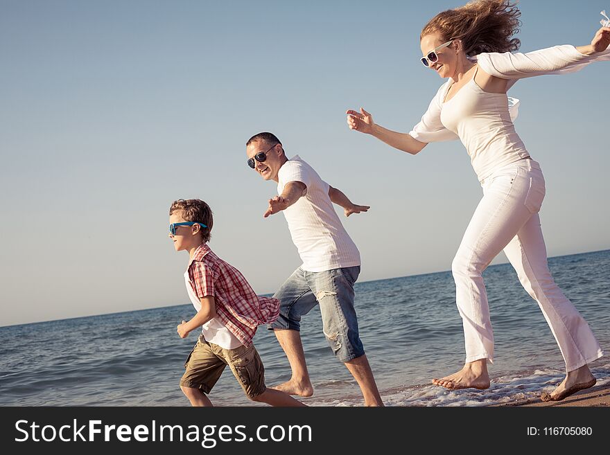 Happy family running on the beach at the day time. People having fun outdoors. Concept of summer vacation and friendly family.