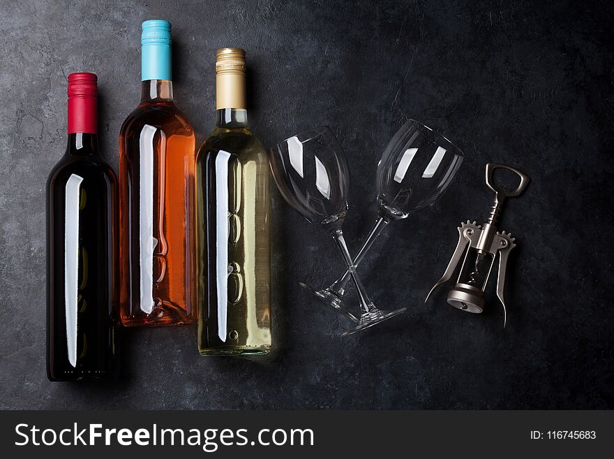Red, rose and white wine bottles with wine glasses and corkscrew on stone table. Top view
