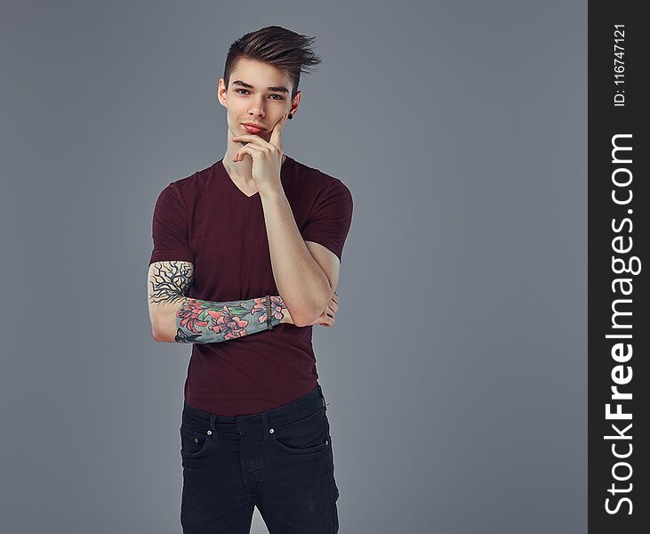 Handsome fashionable pensive guy with stylish hair and tattoo on his arm posing in a studio. on a gray background. Handsome fashionable pensive guy with stylish hair and tattoo on his arm posing in a studio. on a gray background.